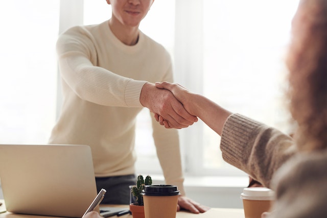 two-people-at-opposite-ends-of-a-desk-shaking-hands